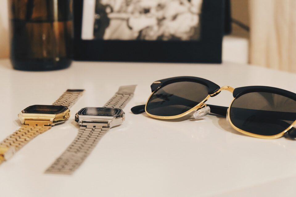 2 expensive timepieces on table next to sunglasses